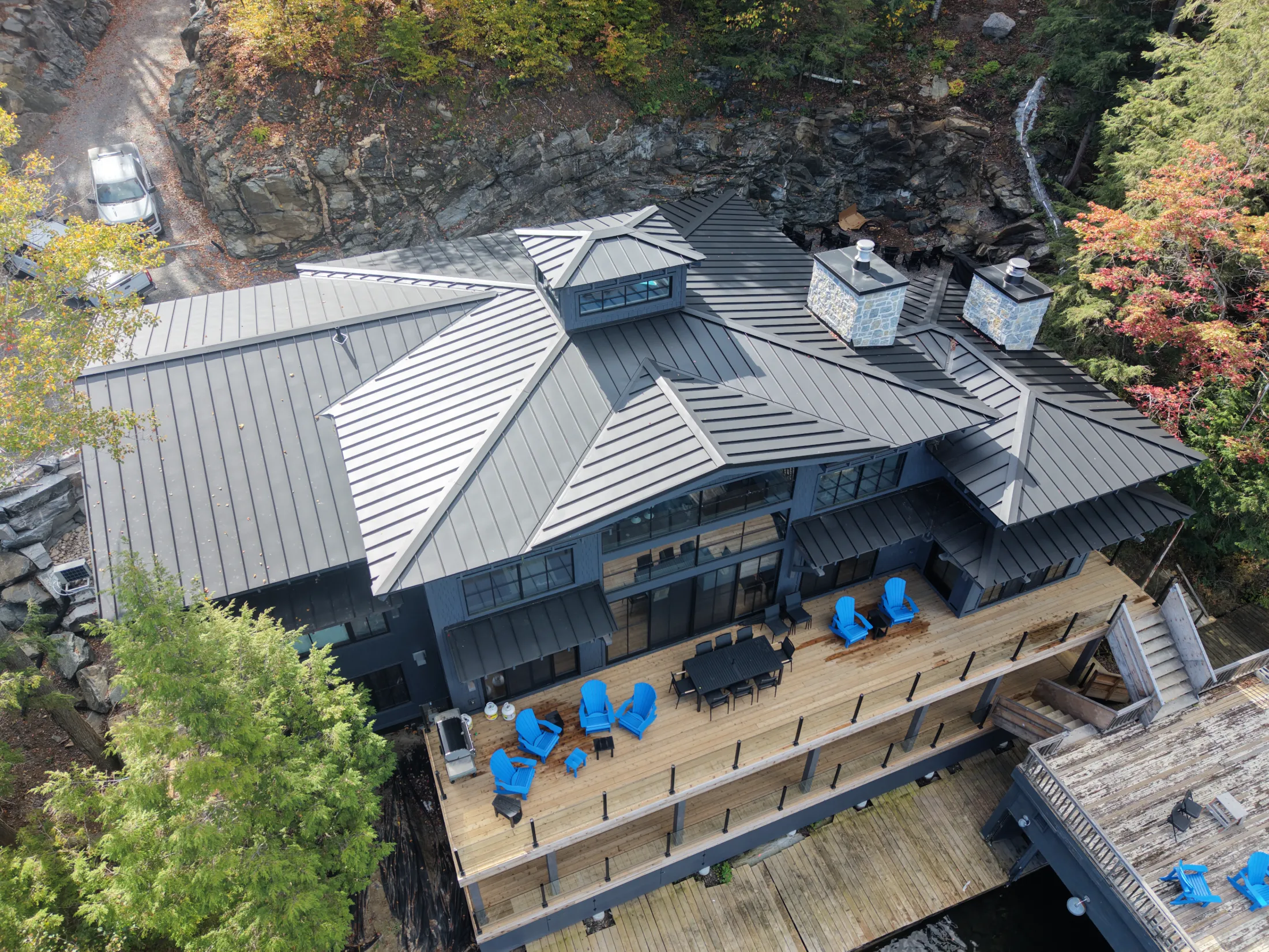 Custom standing-seam metal roof on a lakeside home, with intersecting rooflines and stone chimneys